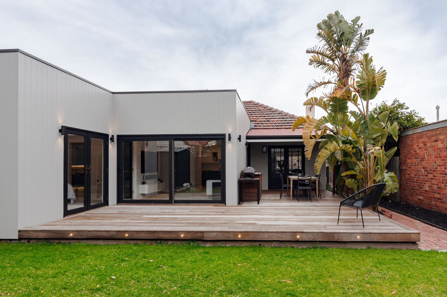 Modern single-story house with wooden deck, palm trees, and large glass windows.
