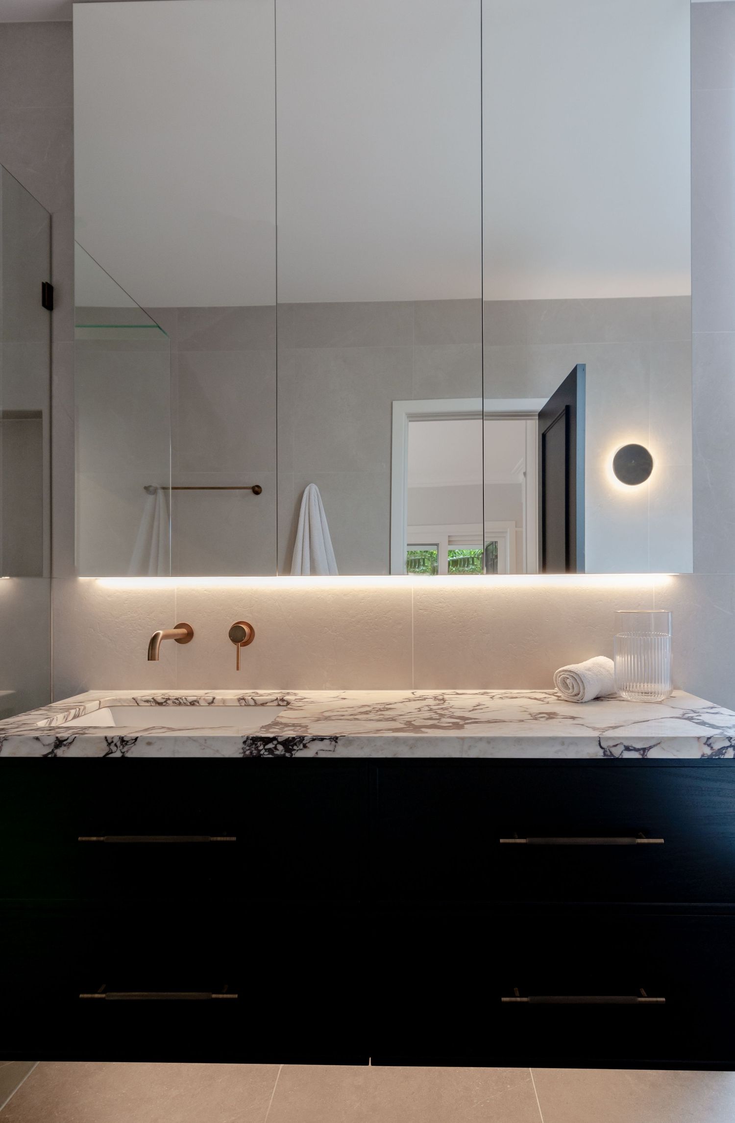 Luxury bathroom vanity with marble countertop, black cabinets, and backlit mirror.