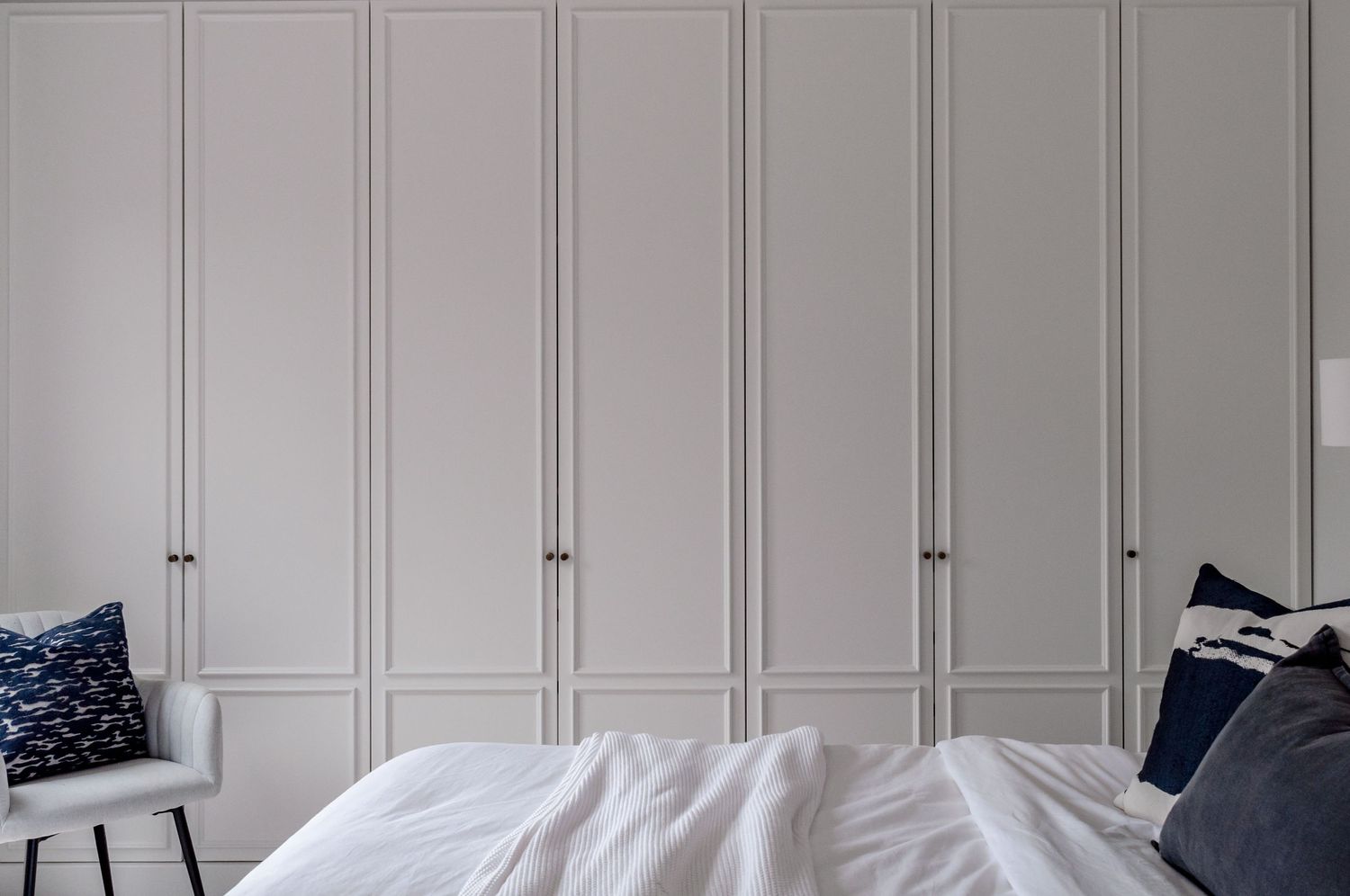 White built-in wardrobes with panel details and navy blue accents in a modern bedroom.