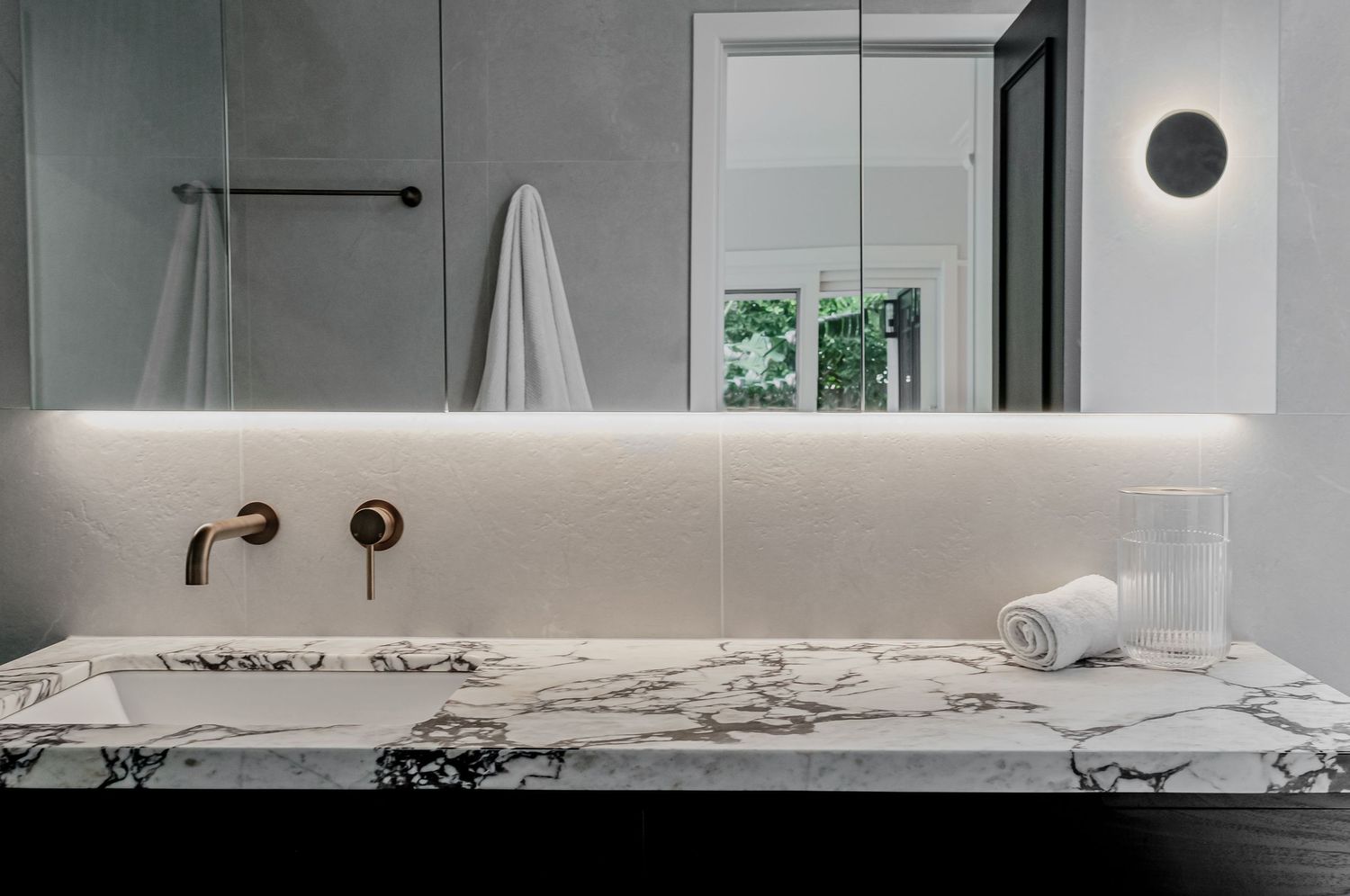 Close-up of marble bathroom vanity with brass wall-mounted faucet and modern lighting.