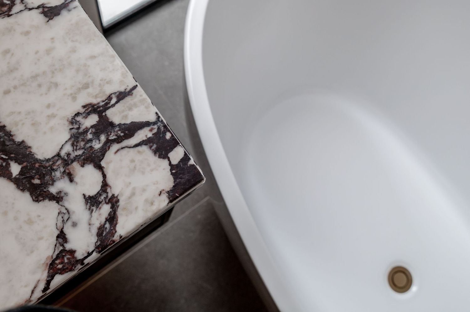 Detail shot of white bathtub edge against marbled surface showing contrasting textures.