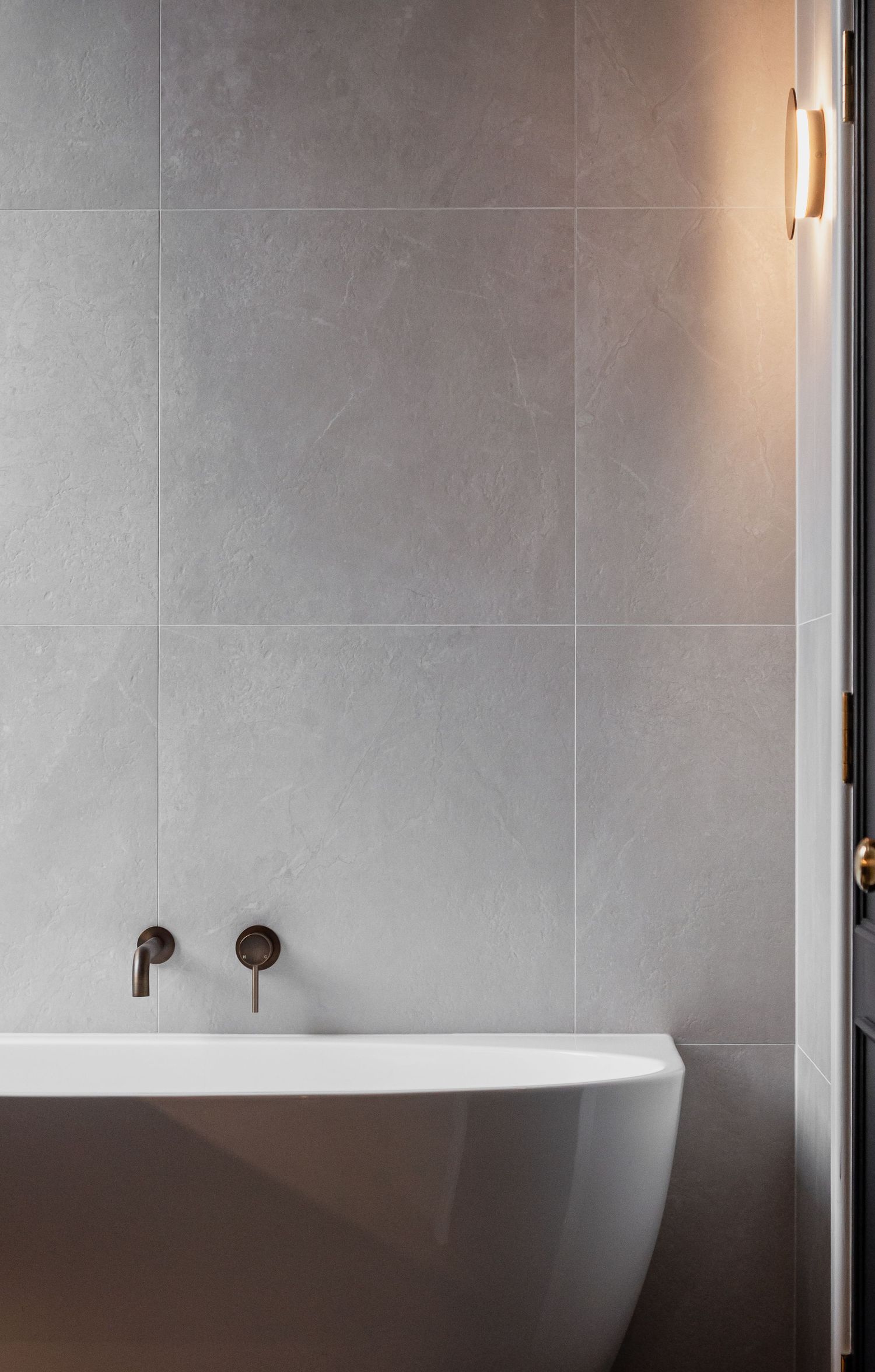 Contemporary bathroom with freestanding white tub against grey tiled walls.