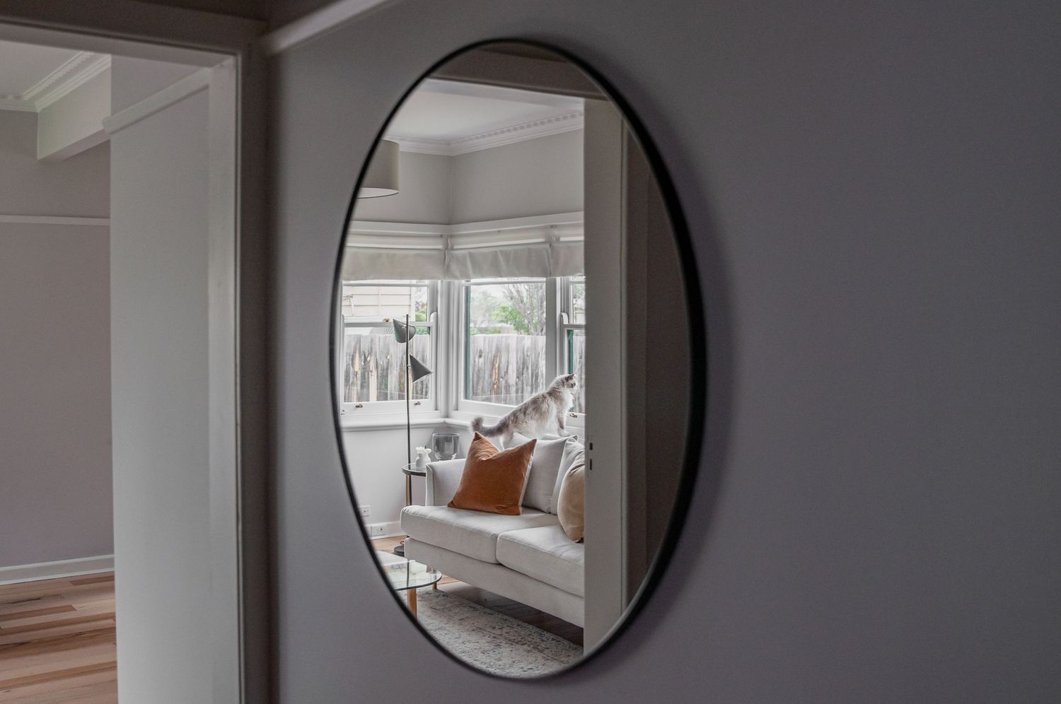 Round black-framed mirror reflecting bright interior living space.