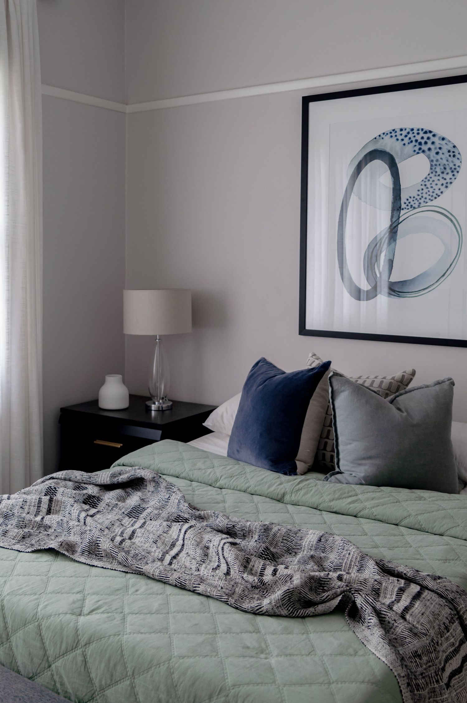 Cozy bedroom with sage green bedding and abstract blue artwork above the headboard.