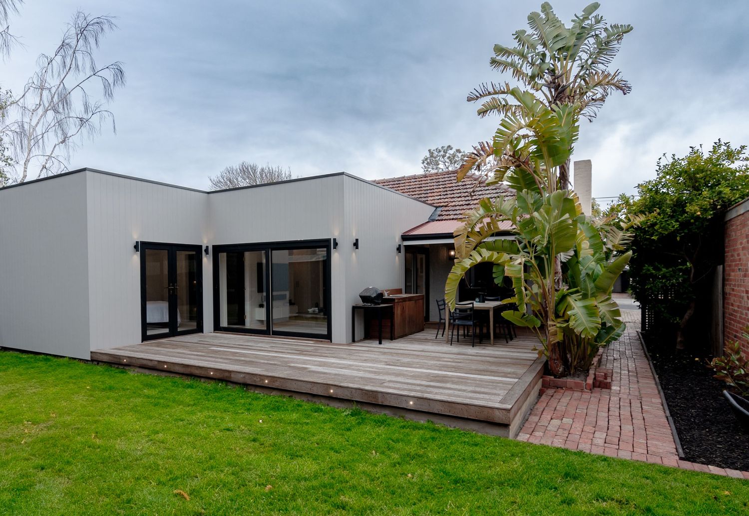 Modern white house exterior with wooden deck and lush garden landscaping.