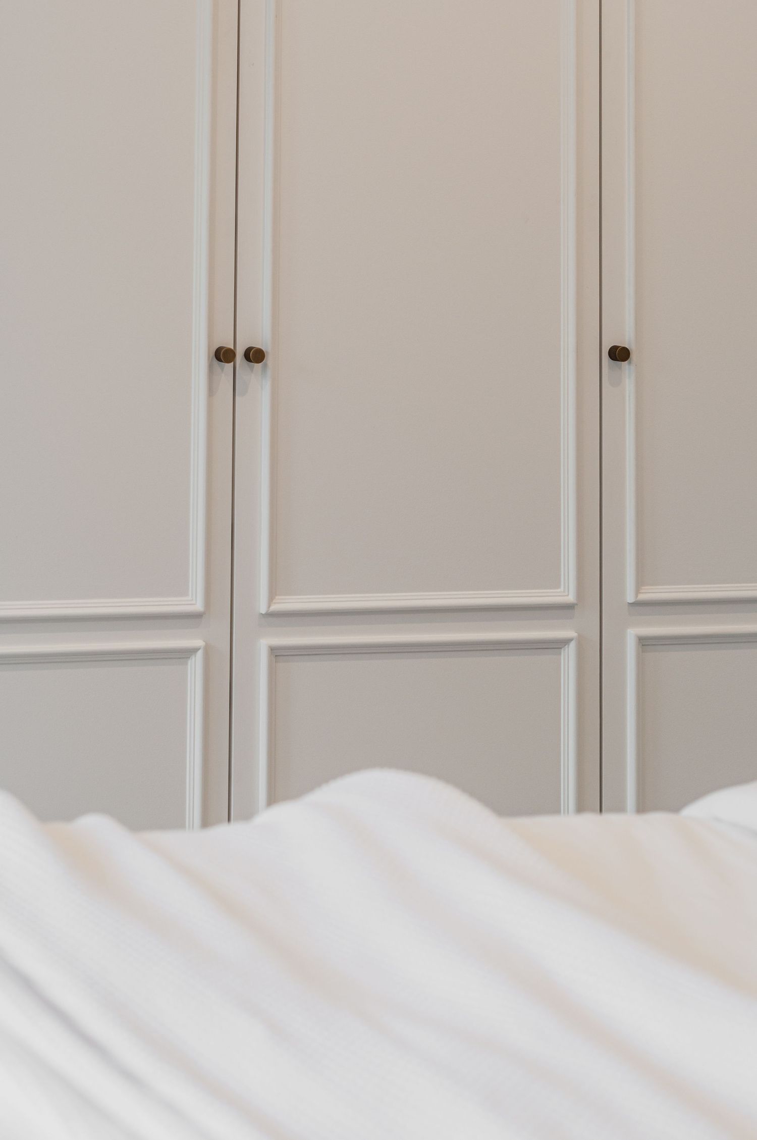 Close-up of white paneled wardrobe doors with brass knobs against neutral wall.