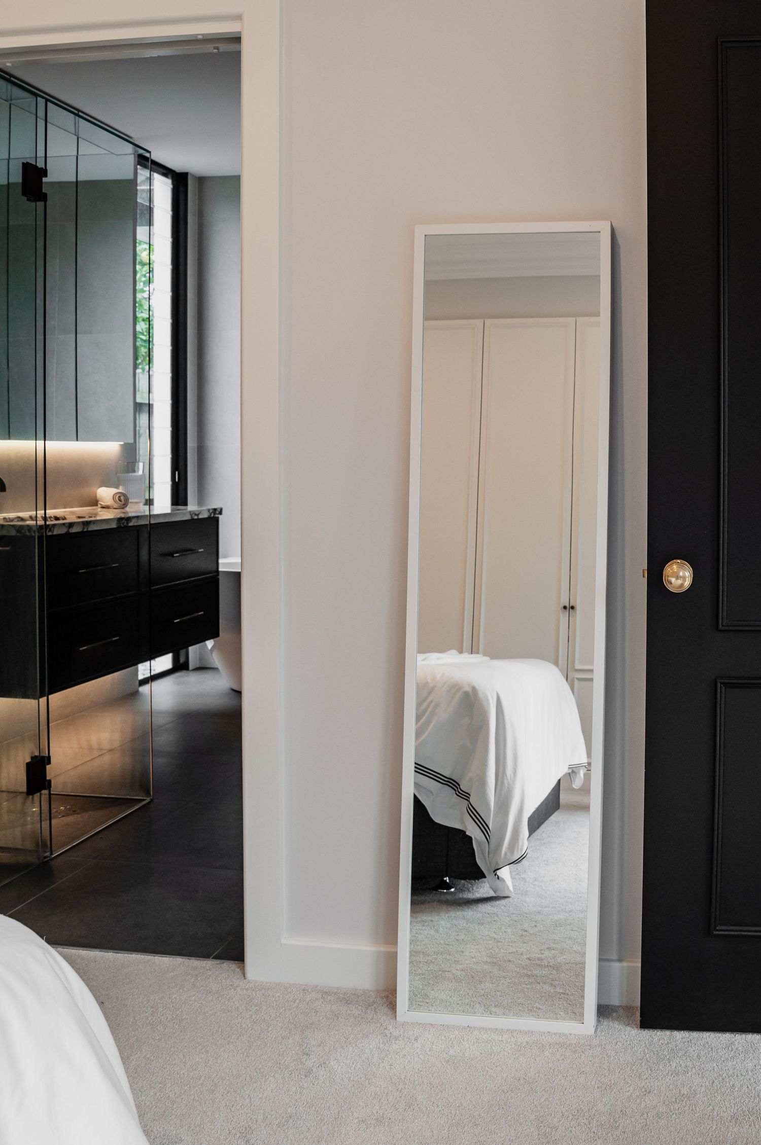Contemporary bedroom with full-length mirror and black accents showing bathroom reflection.