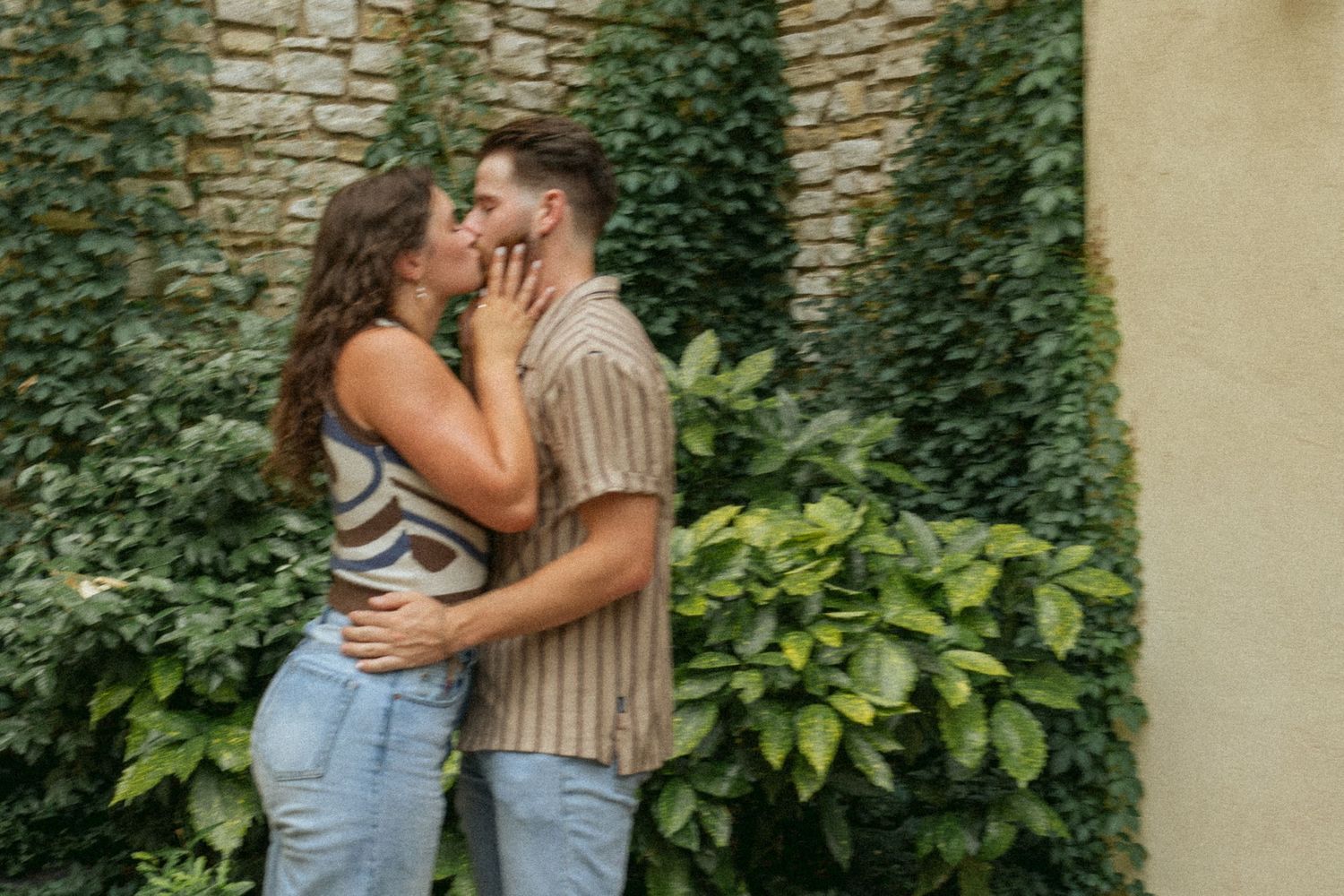 Romantic embrace against ivy-covered stone wall in summer garden setting.
