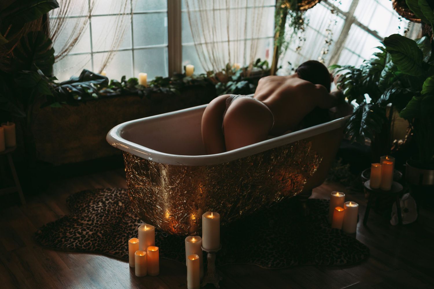 Woman nude in a vintage bathtub, arching her back, surrounded by candles and soft lighting, highlighting her curves and confidence.