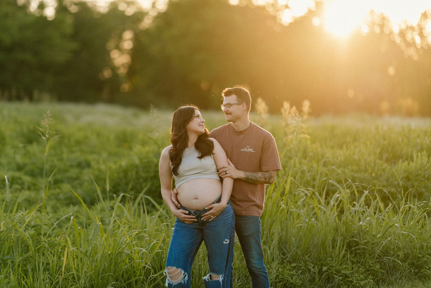 Golden sunset illuminates couple during outdoor maternity photography session in grassy field.