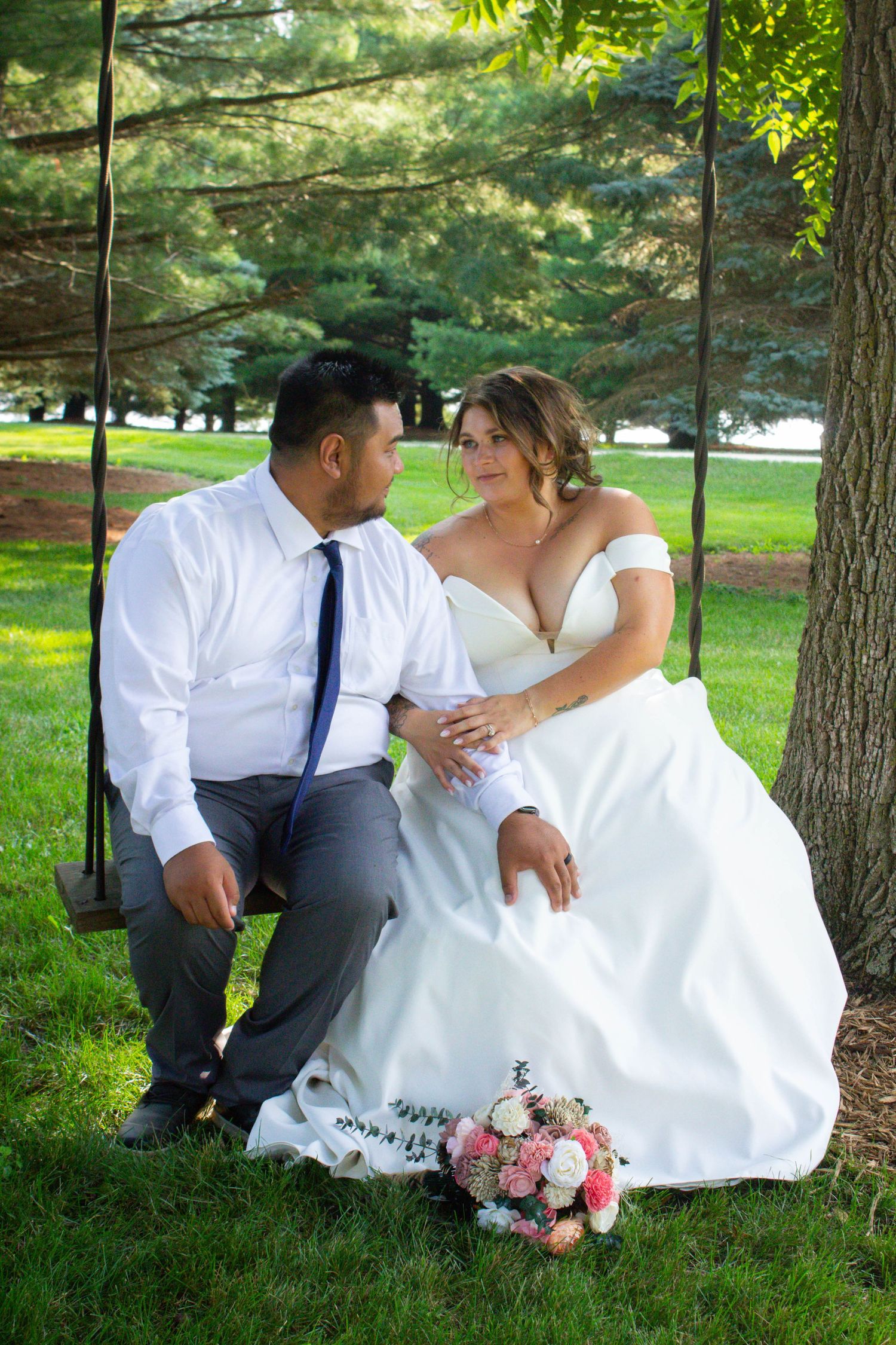 Romantic couple sitting under pine trees with pink floral bouquet.