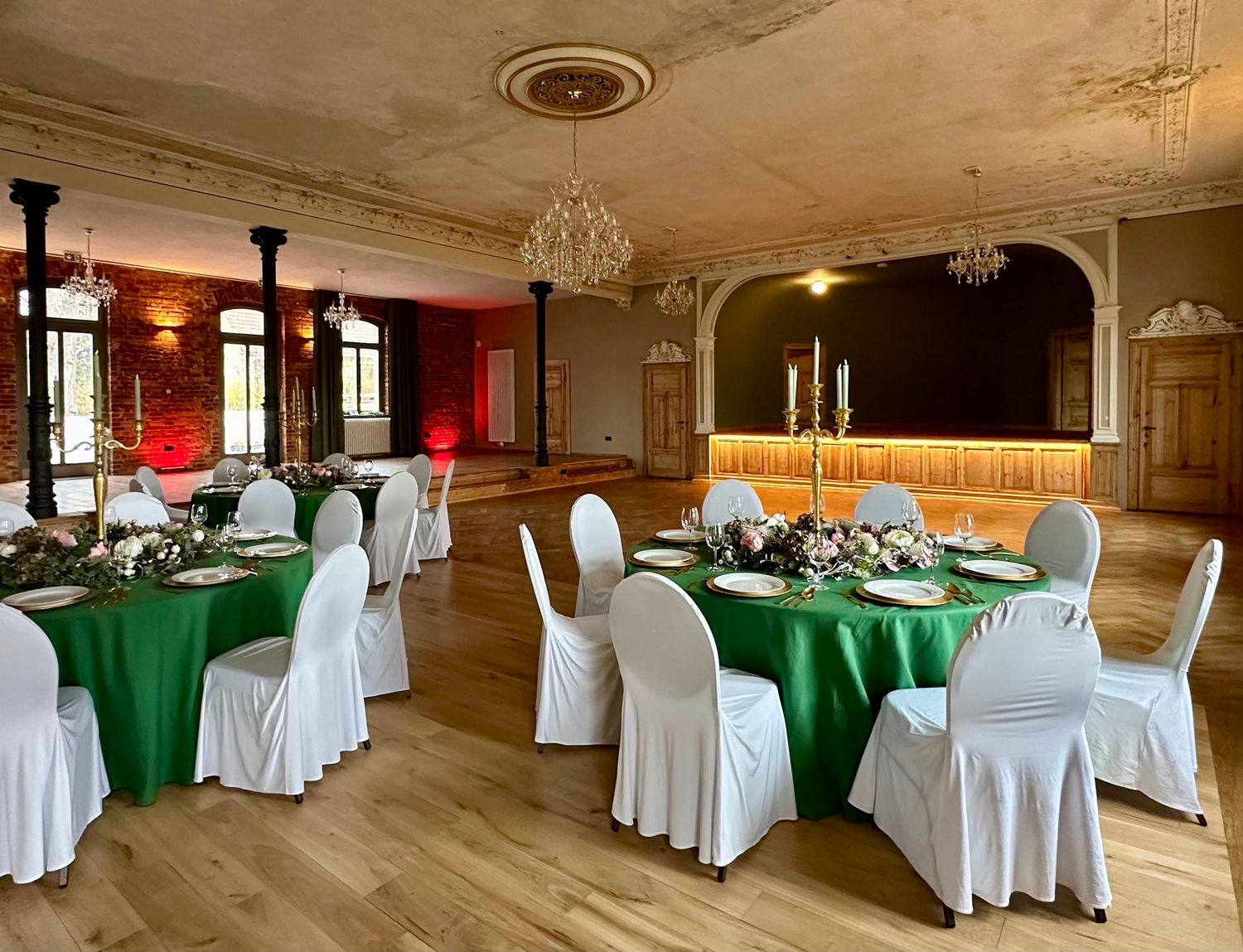 Elegant banquet hall with ornate trim features round tables covered in green tablecloths and white chair covers.