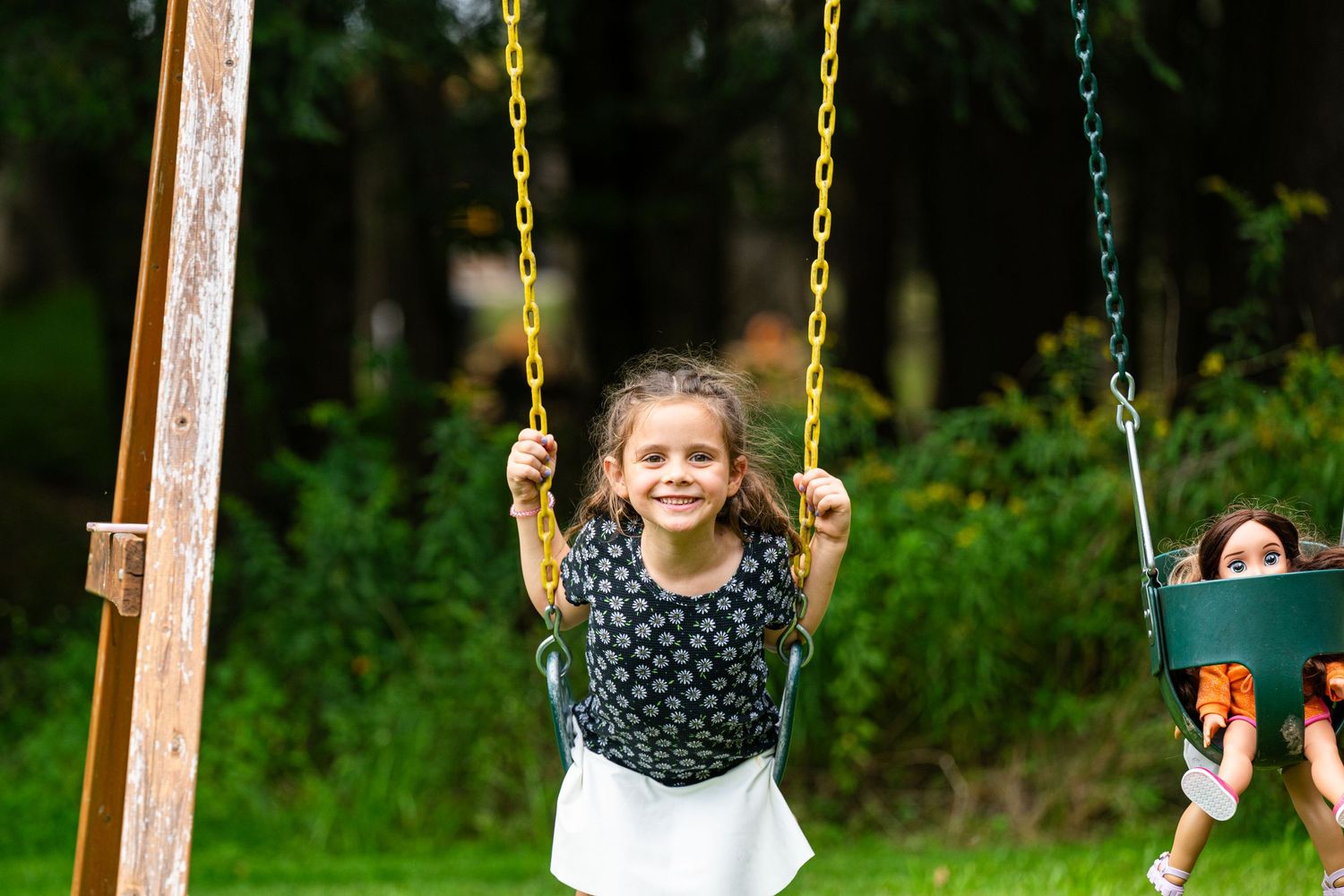 Children enjoying swings at a playground set against green foliage background.