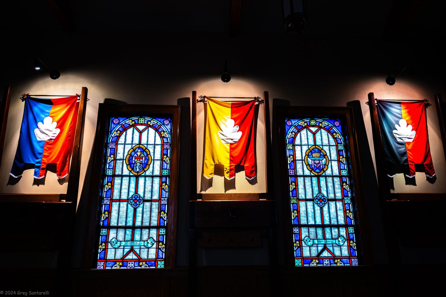 Row of illuminated stained glass windows in a dark church or cathedral.