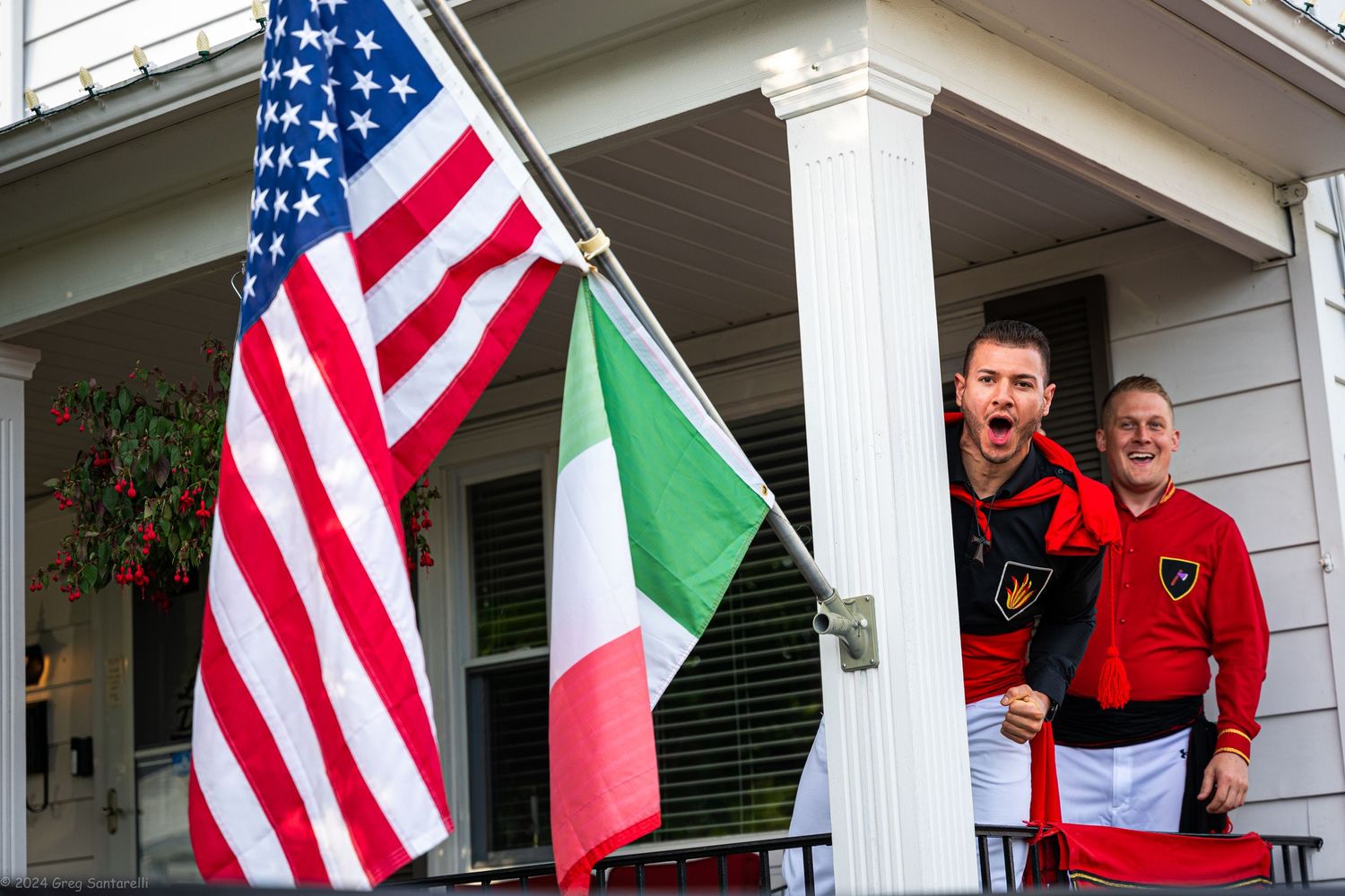 American and Italian flags displayed on a white porch with uniformed personnel.