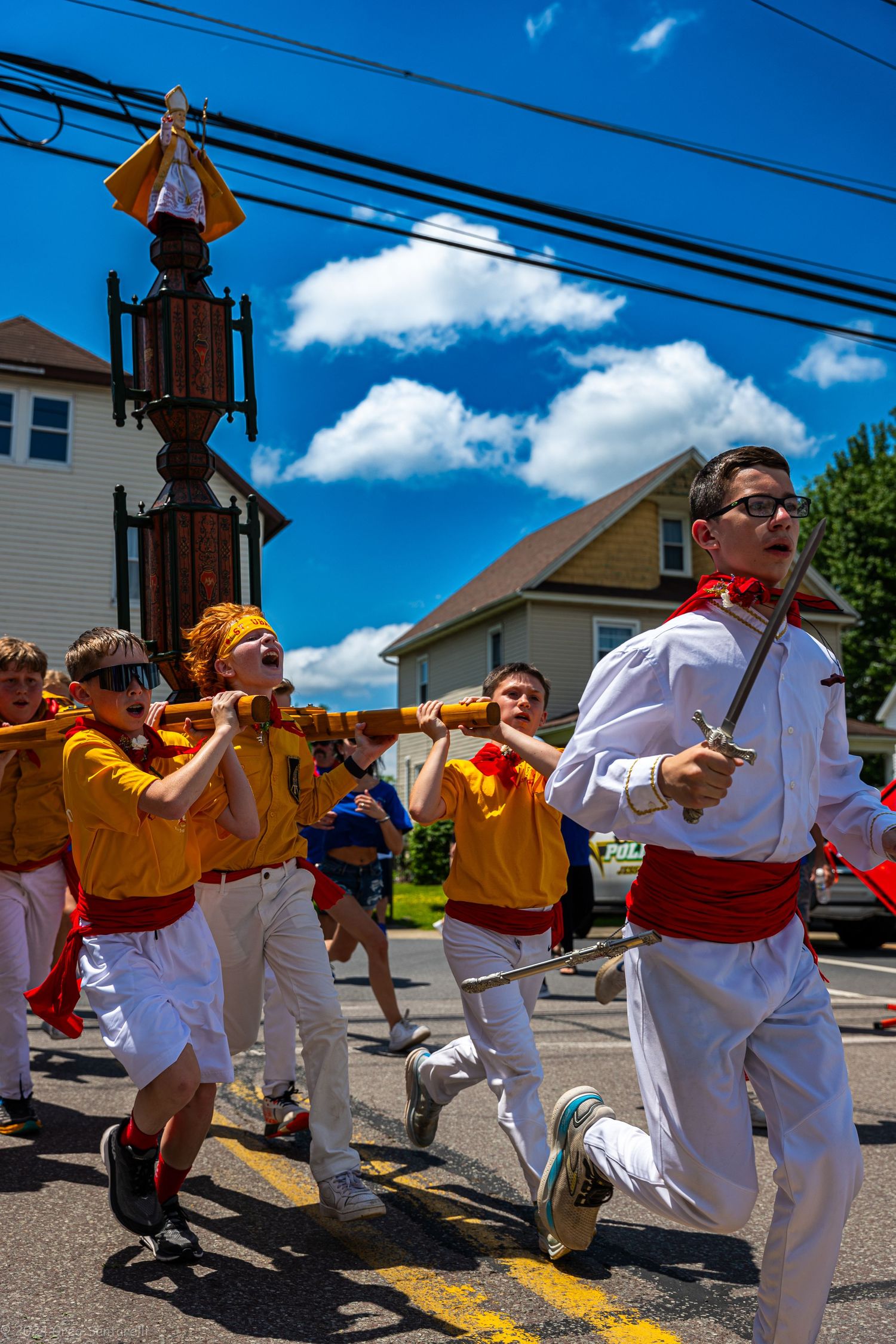 Performers in white and yellow costumes dancing in a line on a sunny street.