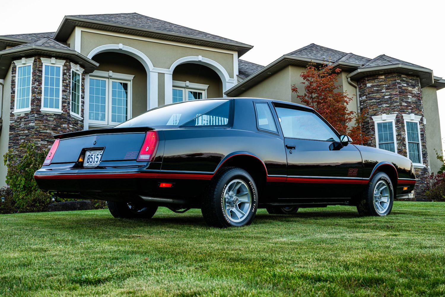 Wide panoramic view of a black vintage car displayed on manicured lawn near luxury homes.