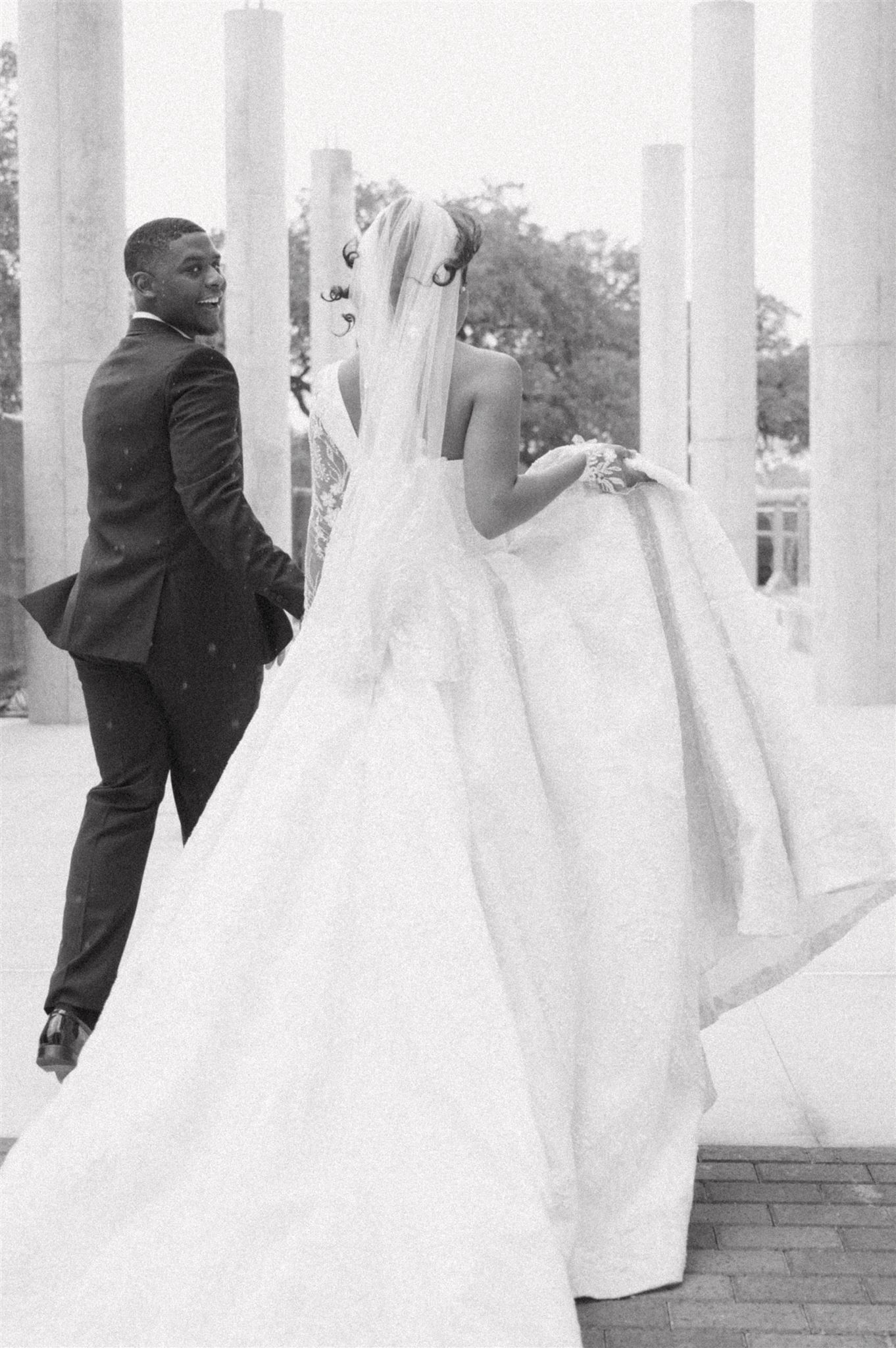 Black and white wedding photo showing a couple in formal attire standing between classic white columns.