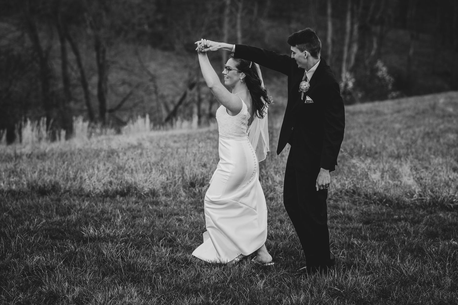 A black and white wedding photo of a couple dancing on a hillside.