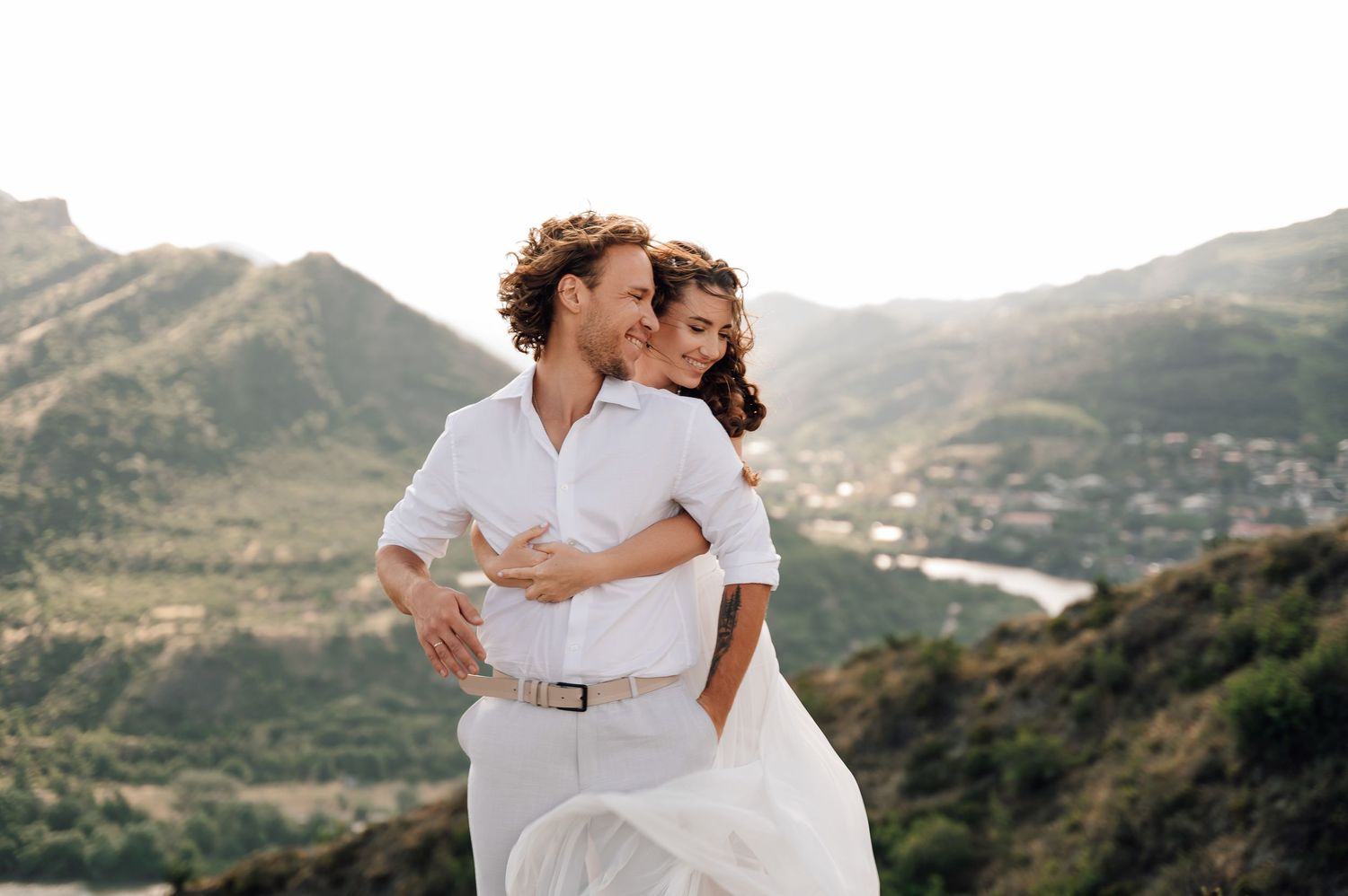Romantic photoshoot with white outfits against a mountainous landscape backdrop.