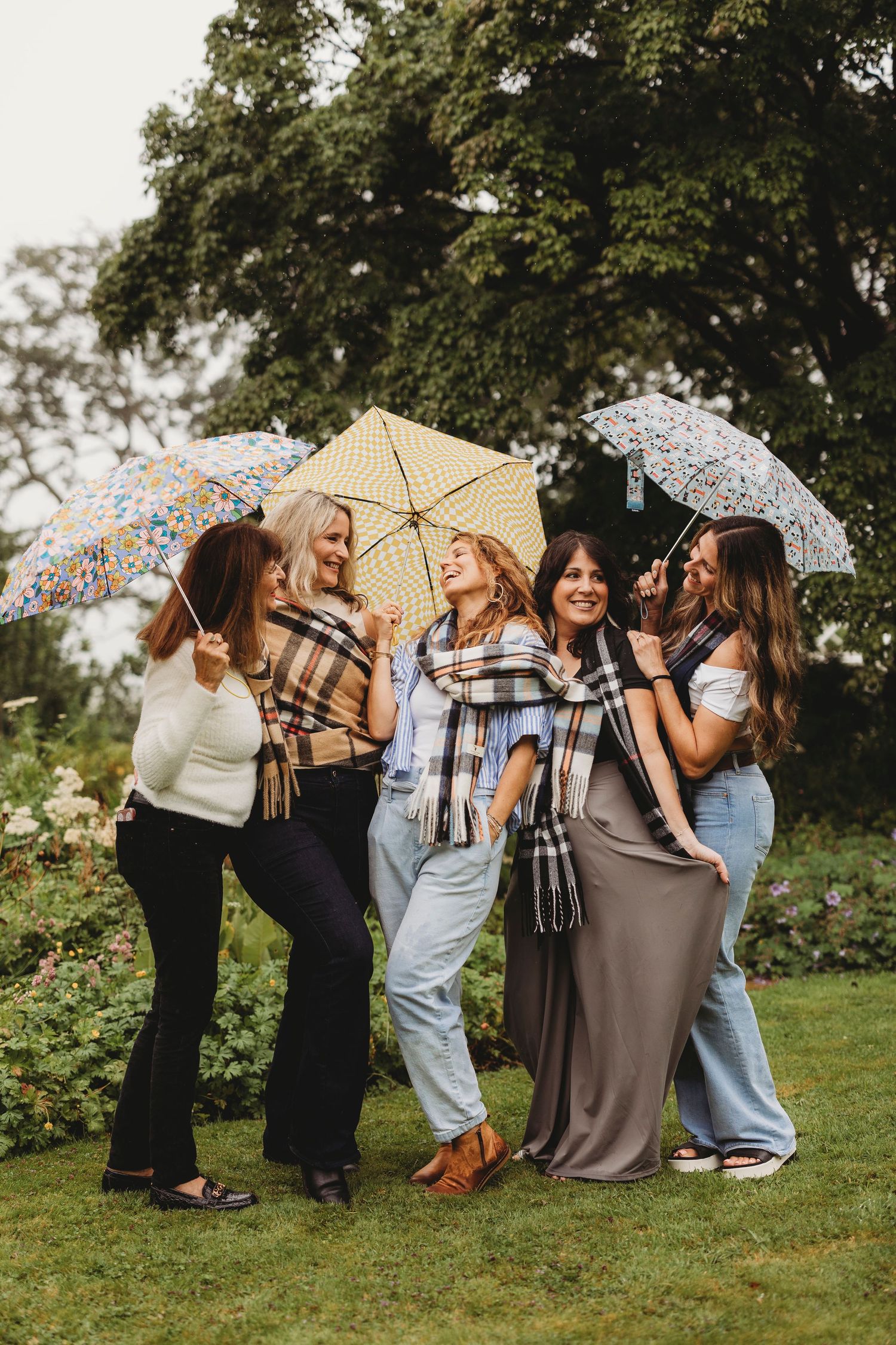 A group of friends with umbrellas laughing together in a garden setting.