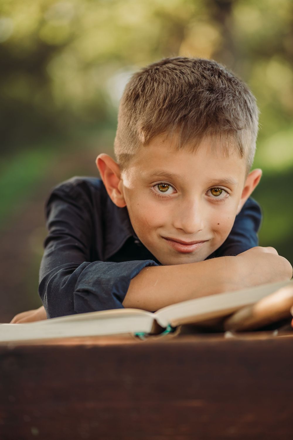 Young student rests head on wooden desk in outdoor nature setting.