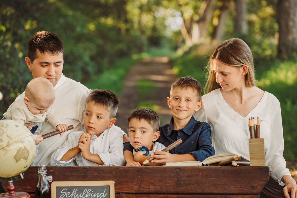 Family gathers around rustic desk in forest setting for back to school themed photo.