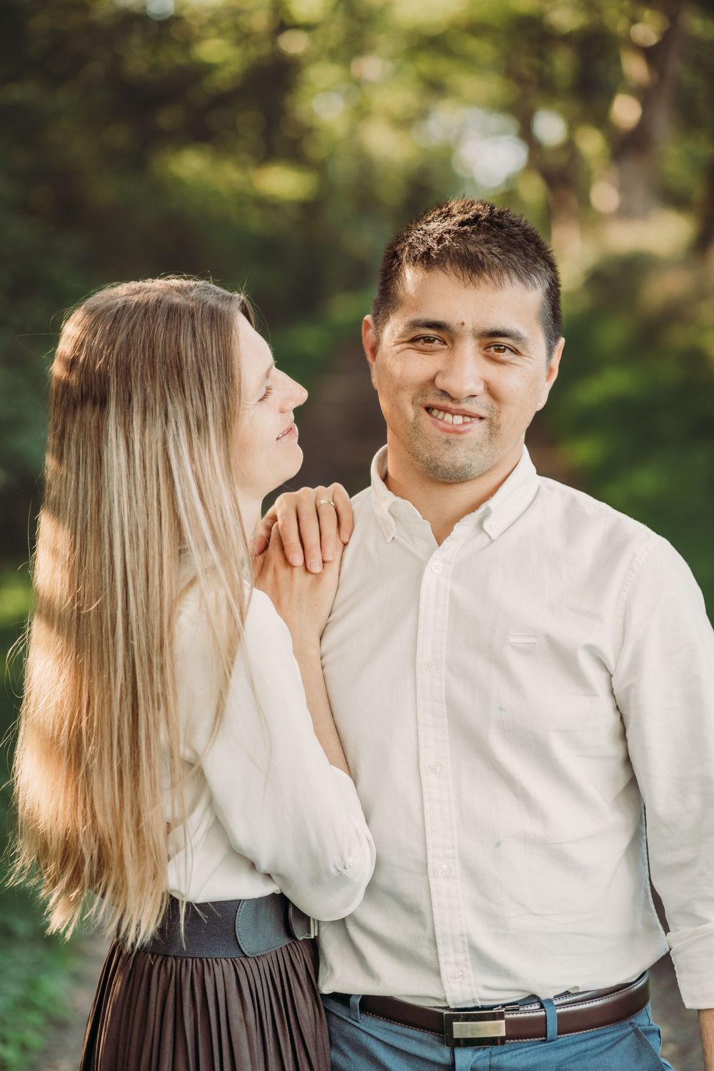 Couple in white shirts standing close together in a wooded setting.
