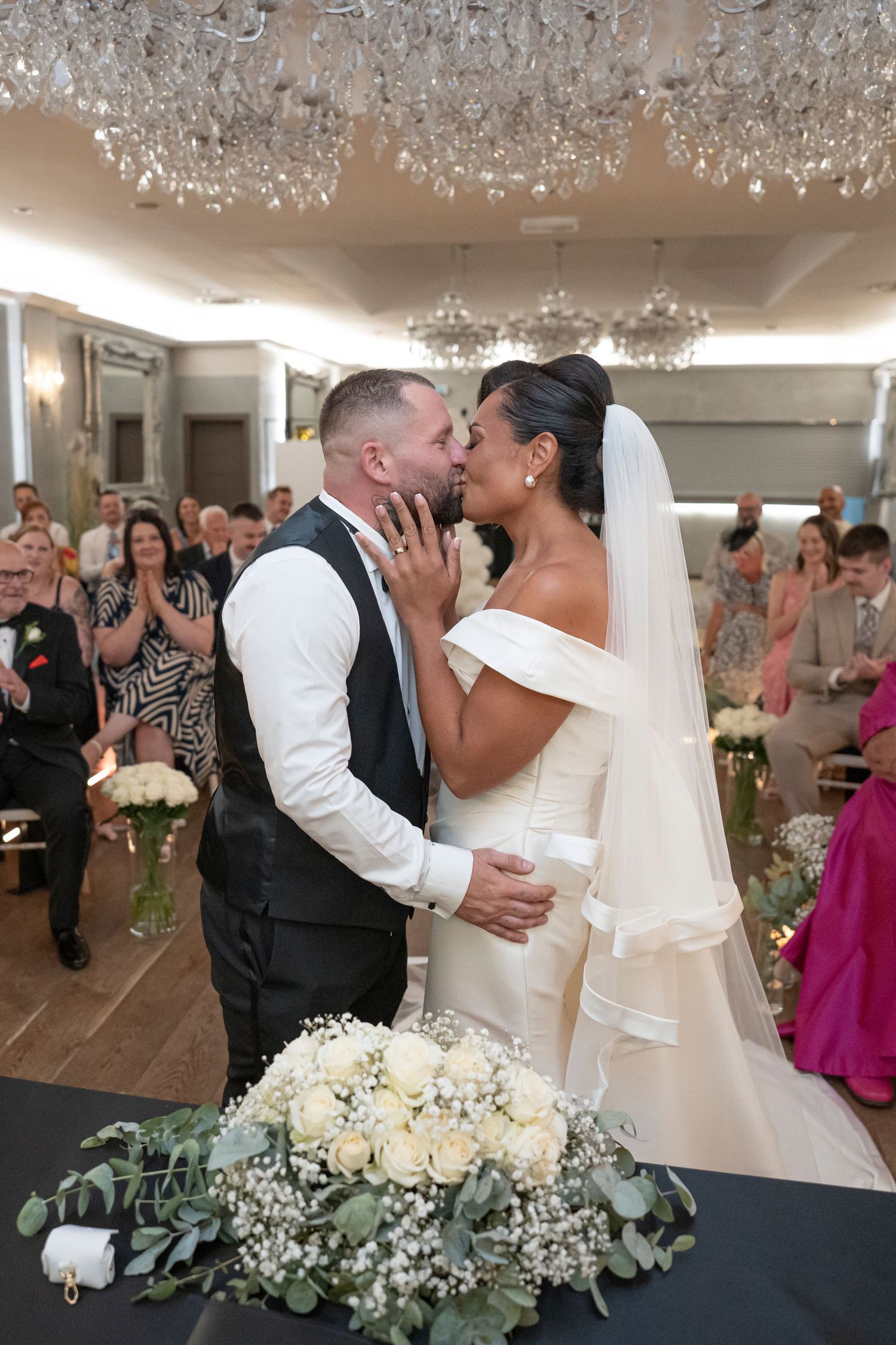 An elegant wedding reception scene with crystal chandeliers and white floral centerpieces.