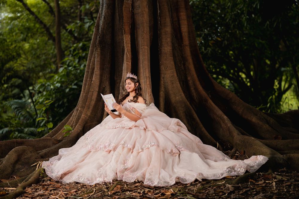 A dramatic pink ballgown photographed against massive tree trunks in a forest setting.