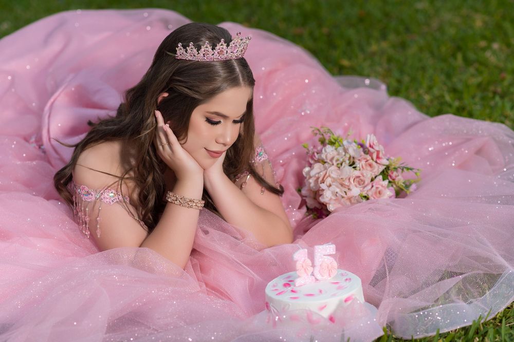 A pink quinceañera dress spread out on green grass during a photo session.