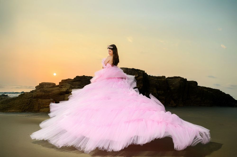 A flowing pink tulle dress photographed at sunset against a rocky beach landscape.
