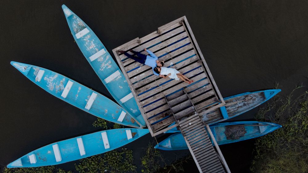 Romantic couple shares a tender moment on a dock with blue boats in the background at sunset.