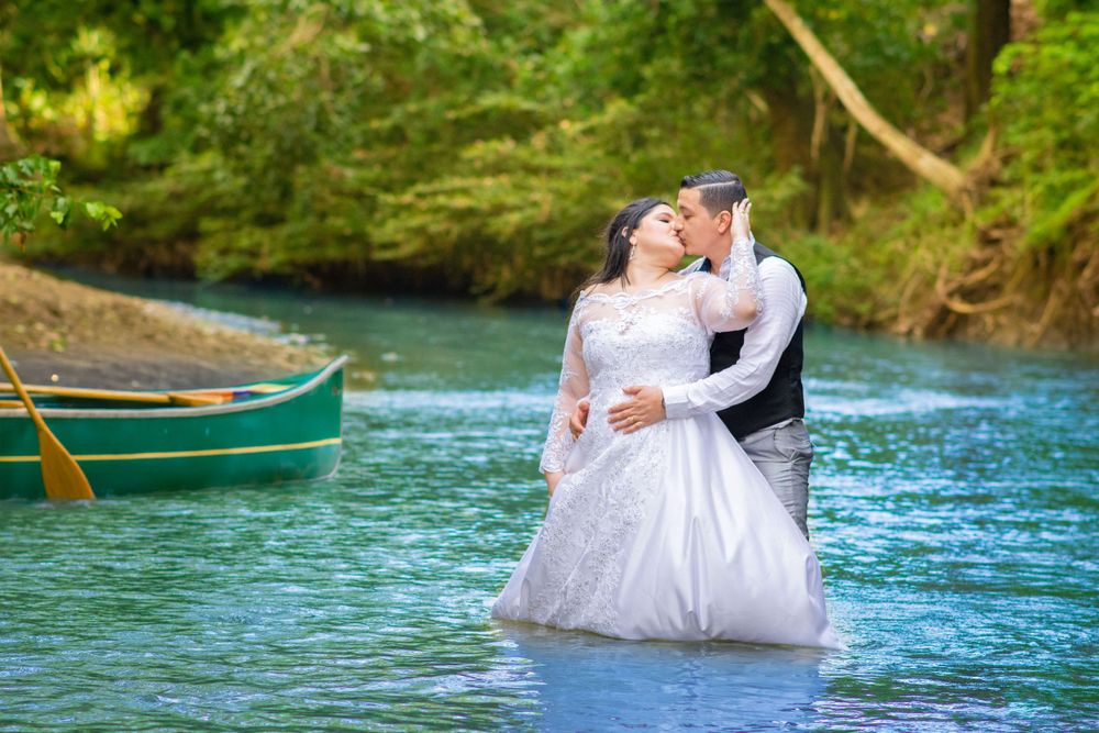Couple in wedding attire sitting in canoes on turquoise water surrounded by lush greenery.