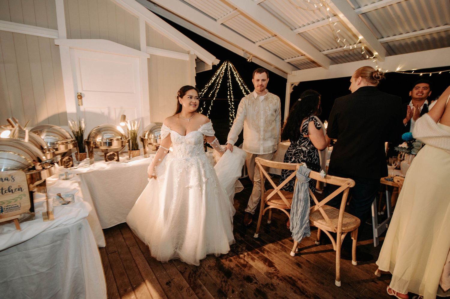 Elegant wedding reception setup in rustic indoor venue with wooden chairs and white decor.