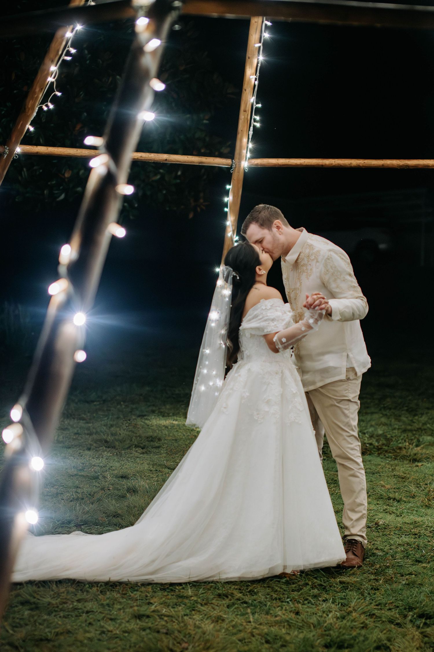 Intimate wedding moment captured under illuminated tent poles at night.