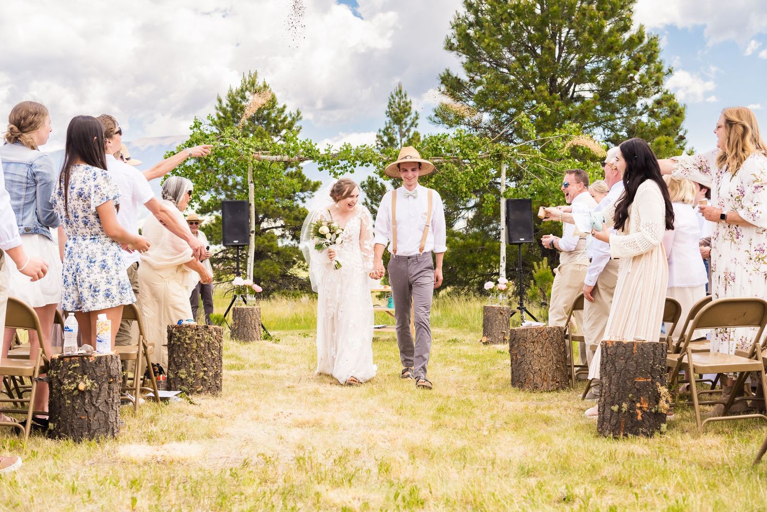 An outdoor wedding ceremony in a field with guests celebrating and throwing petals.