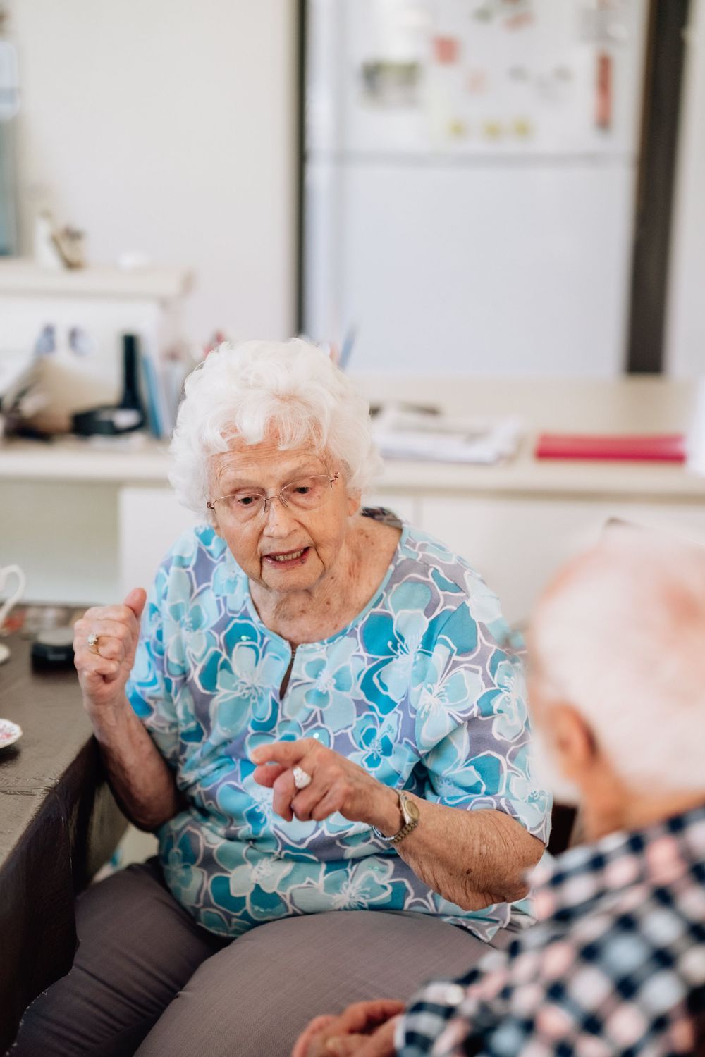 An elderly woman sitting, telling a story to an elderly man.