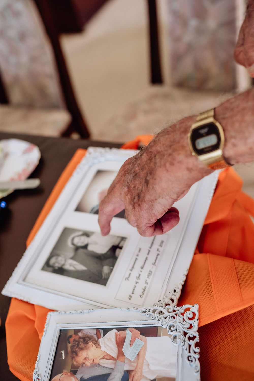 The hand of an elderly man, pointing at old wedding photos.
