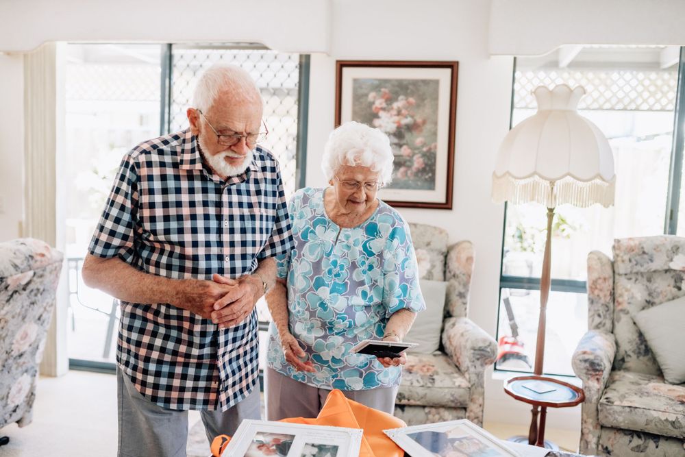 An elderly man and woman stand next to a table looking at old photos.