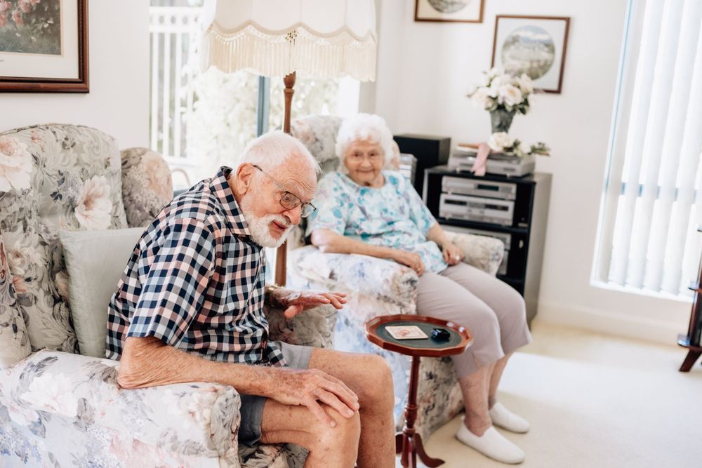 An elderly man and woman share stories while sitting in arm chairs.