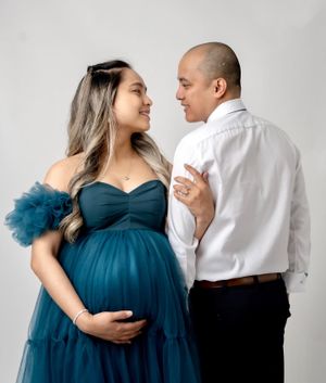 Studio maternity portrait featuring a teal tulle gown and intimate couple pose.