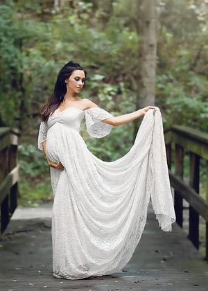 Woman in elegant white lace dress poses on wooden bridge surrounded by trees.