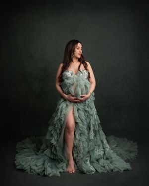 Artistic maternity portrait with dramatic sage green tulle dress in moody studio setting.