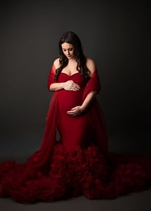 Dramatic maternity photoshoot featuring a flowing red ruffled gown against a dark background.