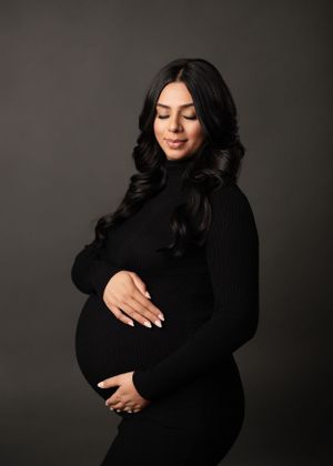 Artistic maternity photoshoot featuring elegant black dress against dark backdrop.