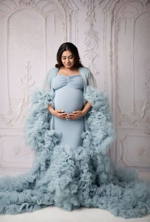 Maternity portrait in powder blue gown with dramatic tulle details against ornate white backdrop.
