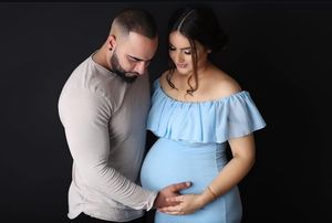 Intimate maternity portrait against black background with couple in casual attire.