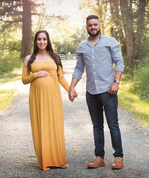 Outdoor maternity photo of couple walking hand-in-hand on a forest path.