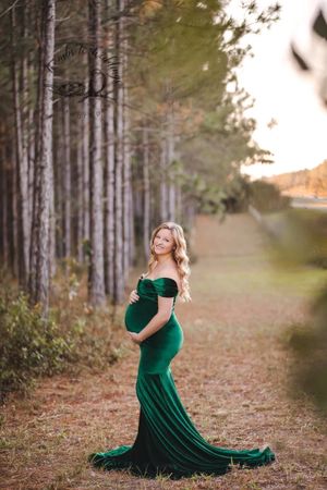 Elegant maternity portraits in an emerald green velvet gown among tall pine trees.